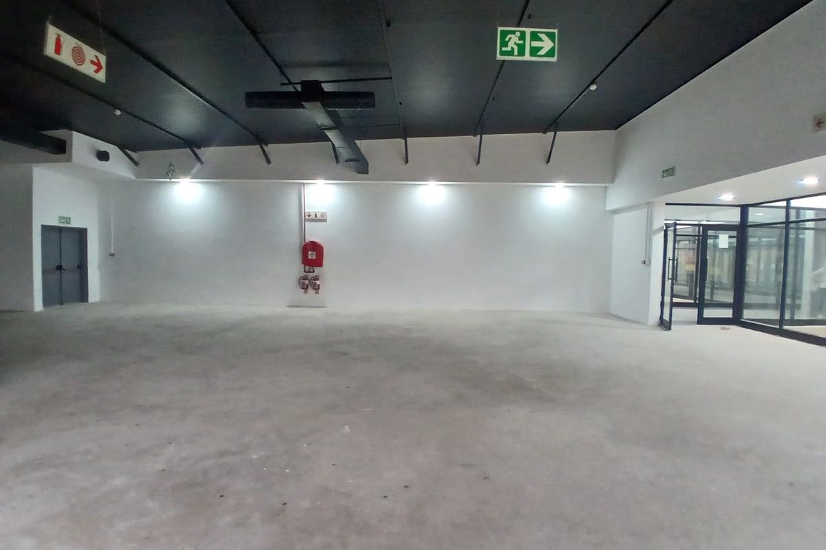 A spacious, open-plan retail unit featuring an exposed ceiling, polished concrete flooring, and integrated emergency safety fixtures, ready for custom fit-out.
