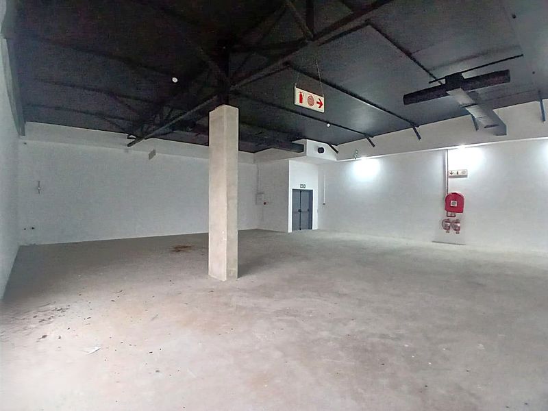 A spacious, open-plan retail unit featuring an exposed ceiling structure, concrete flooring, and essential fire safety equipment.