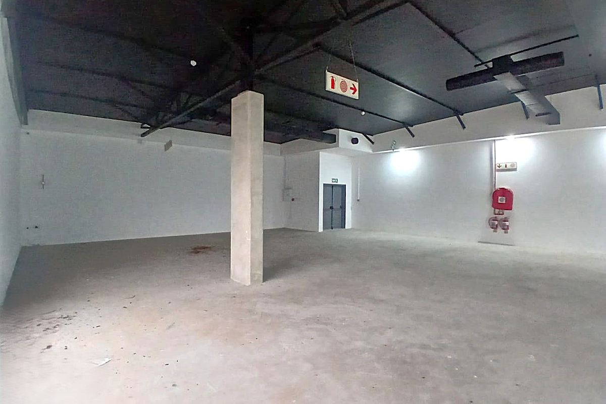 A spacious, open-plan retail unit featuring an exposed ceiling structure, concrete flooring, and essential fire safety equipment.