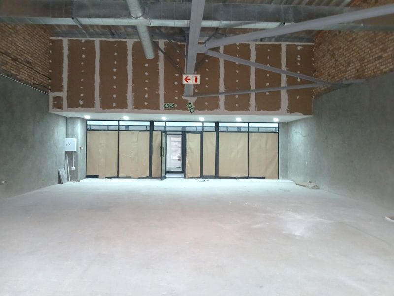 Spacious open-plan retail unit in shell condition, featuring exposed industrial ceilings, brickwork, and large glass storefront windows ready for custom fit-out.