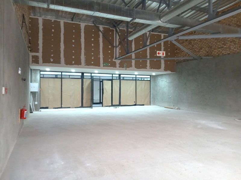 A spacious, unfinished retail unit featuring exposed industrial ceilings, concrete flooring, and a large glass storefront, ready for custom fit-out.