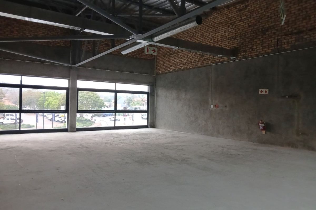 An open-plan industrial retail space featuring exposed brick walls, concrete flooring, high steel roof trusses, and large windows providing ample natural light.