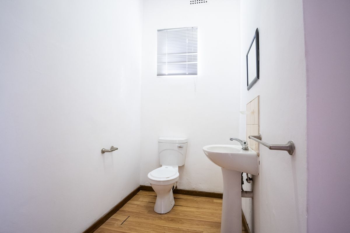 A functional office restroom featuring a pedestal washbasin, toilet, and laminate flooring, providing essential facilities for staff and visitors.