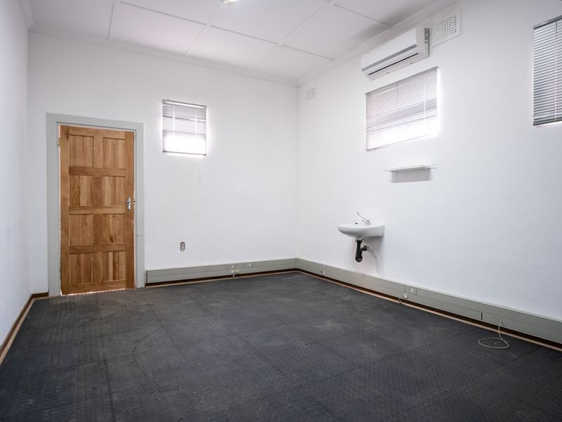 A vacant office space featuring a wall-mounted basin, air conditioning unit, timber door, and durable flooring, suitable for a professional workspace.