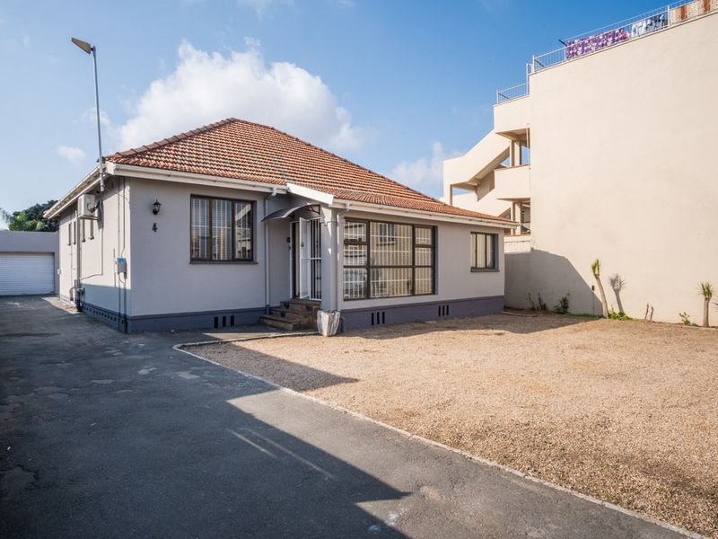 Front view of a single-story office building featuring a tiled roof, paved driveway, and detached garage with security features.
