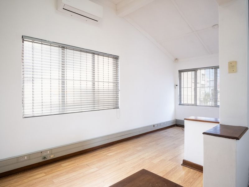A bright, empty office space featuring vaulted ceilings, laminate flooring, split-system air conditioning, and large windows with fitted venetian blinds.