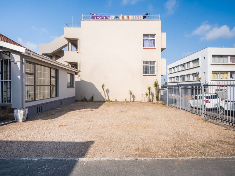 A rear exterior view of the office property featuring a gravel parking or utility area enclosed by metal security fencing.