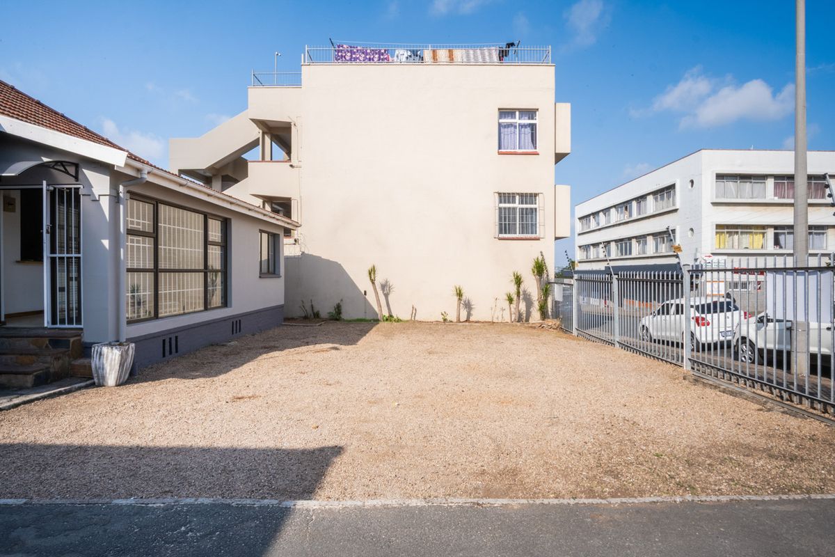 A rear exterior view of the office property featuring a gravel parking or utility area enclosed by metal security fencing.