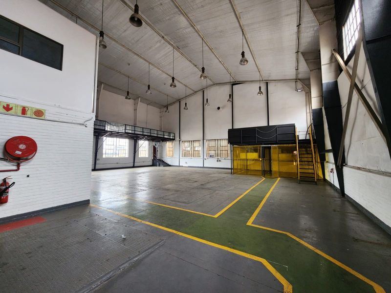 Spacious industrial warehouse unit featuring high ceilings, mezzanine level, steel staircase, and durable painted concrete flooring, suitable for various commercial or storage applications.