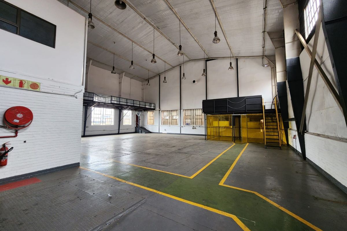 Spacious industrial warehouse unit featuring high ceilings, mezzanine level, steel staircase, and durable painted concrete flooring, suitable for various commercial or storage applications.