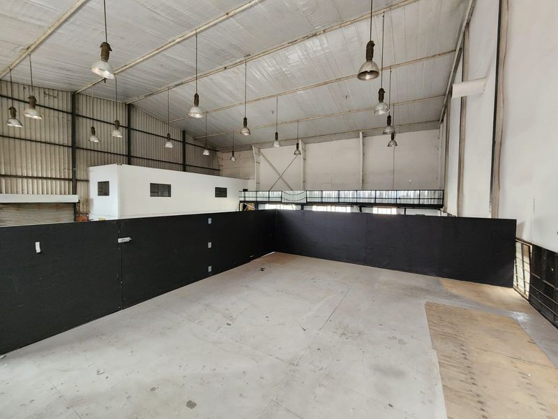Spacious industrial utility area featuring high ceilings with pendant lighting, a mezzanine level, and durable concrete flooring, suitable for various commercial or storage uses.