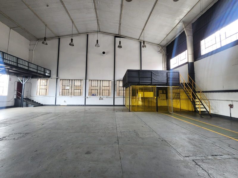 Spacious industrial warehouse area featuring high ceilings, concrete flooring, a mezzanine level with steel staircase, and secure partitioned workspace.