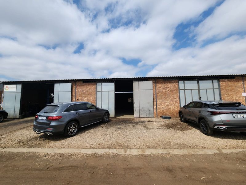 Industrial property exterior featuring a brick facade with multiple large sliding access doors and a gravel driveway area.