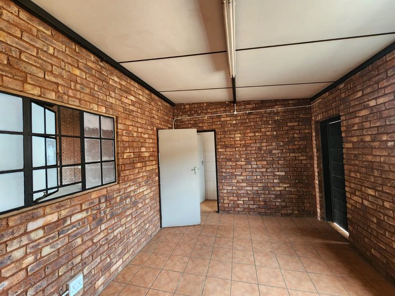 An empty industrial-style office space featuring exposed brick walls, ceramic tile flooring, and functional strip lighting.