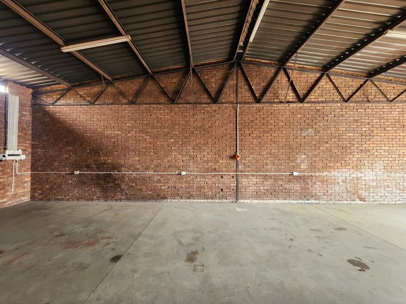 Spacious industrial utility area featuring exposed brick walls, high-clearance metal roof structure, and durable concrete flooring with surface-mounted electrical infrastructure.