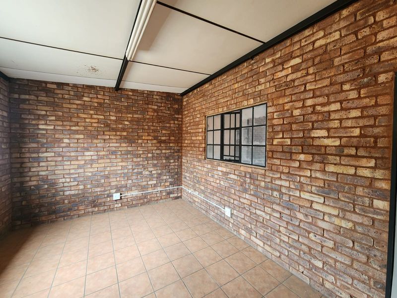 An empty utility space featuring exposed brick walls, tiled flooring, and a steel-framed window, suitable for various industrial or storage applications.