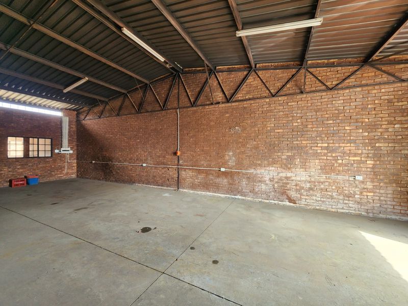 Spacious industrial utility area featuring exposed brick walls, concrete flooring, and high-clearance metal roofing with integrated fluorescent lighting.