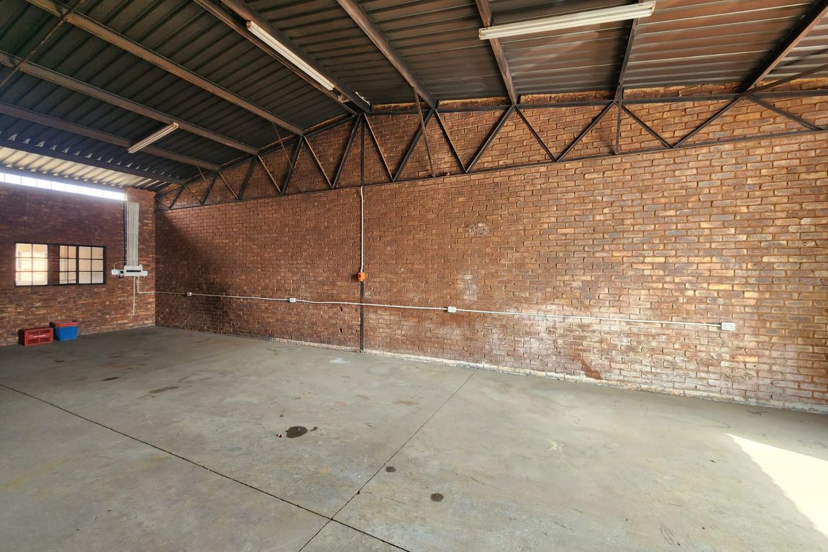 Spacious industrial utility area featuring exposed brick walls, concrete flooring, and high-clearance metal roofing with integrated fluorescent lighting.