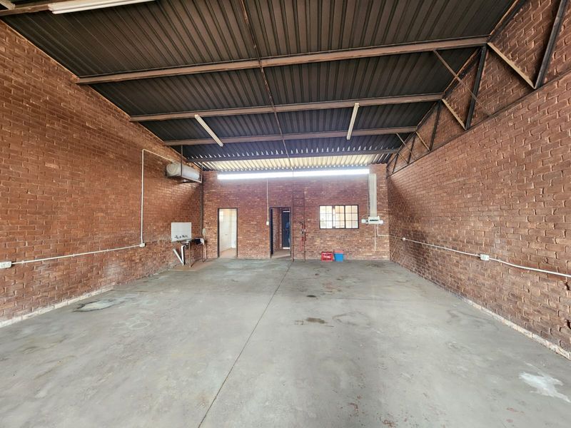 Spacious industrial utility area featuring exposed brick walls, concrete flooring, and a high corrugated metal roof with functional wall-mounted sink and lighting.