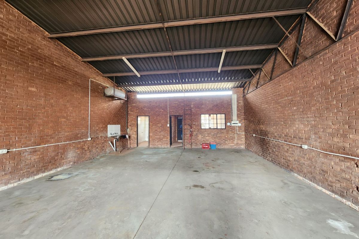 Spacious industrial utility area featuring exposed brick walls, concrete flooring, and a high corrugated metal roof with functional wall-mounted sink and lighting.
