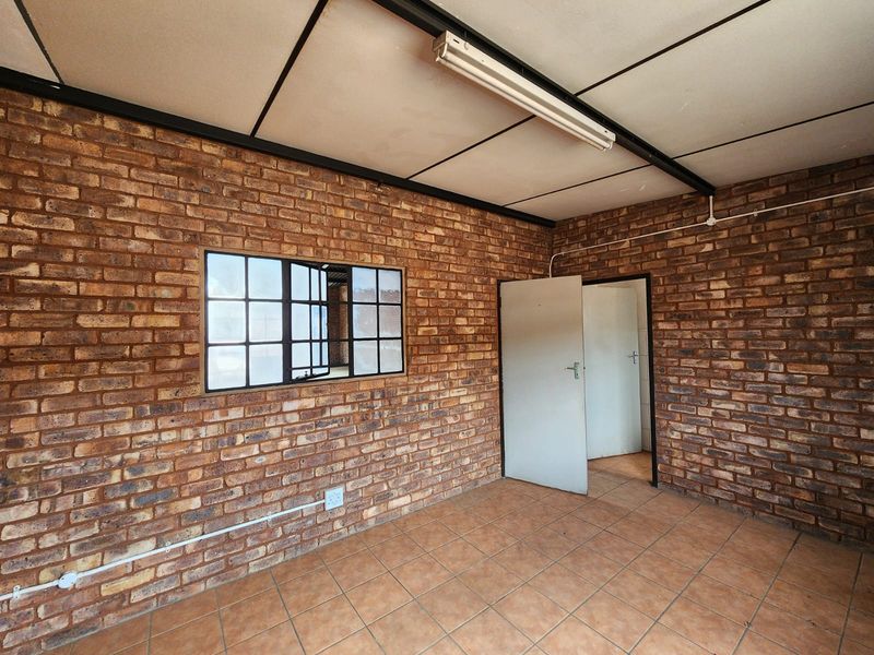 An empty industrial-style office space featuring exposed brick walls, tiled flooring, and a functional grid ceiling with surface-mounted lighting.