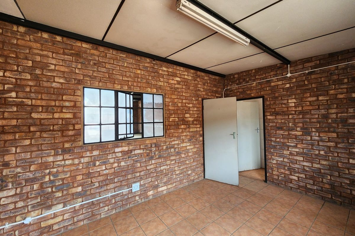 An empty industrial-style office space featuring exposed brick walls, tiled flooring, and a functional grid ceiling with surface-mounted lighting.