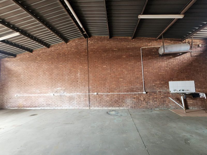 Spacious industrial utility area featuring exposed brick walls, concrete flooring, metal roof structure, and a wall-mounted utility sink with exposed plumbing.