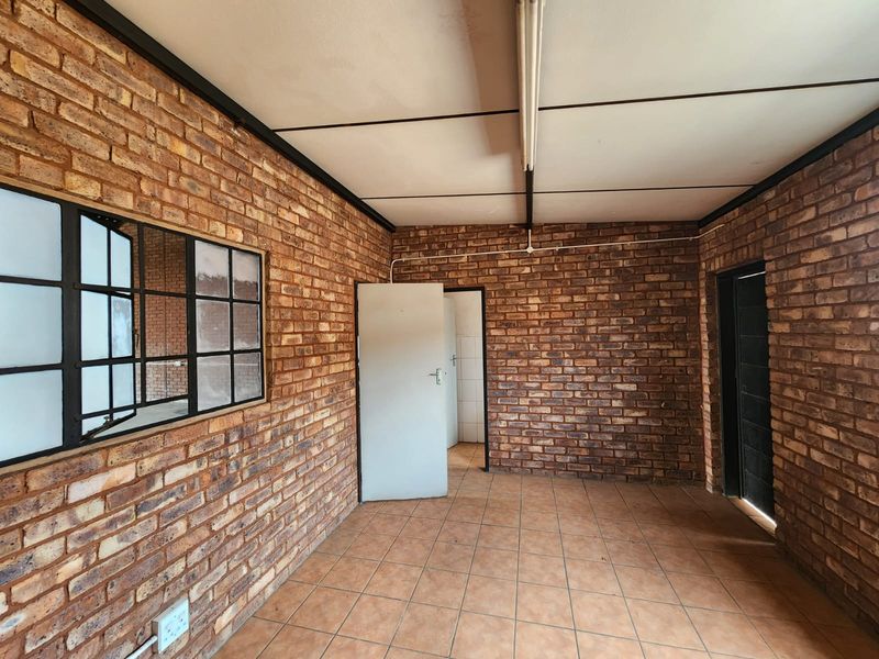 An empty industrial-style office space featuring exposed brick walls, tiled flooring, and functional strip lighting, offering a versatile layout for various business uses.