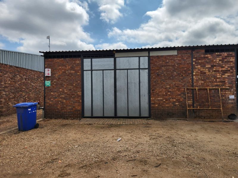 Rear exterior view of an industrial unit featuring exposed brick walls, large metal sliding doors, and a corrugated roof structure.