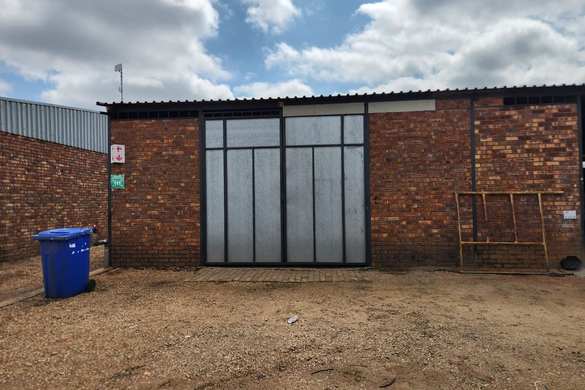 Rear exterior view of an industrial unit featuring exposed brick walls, large metal sliding doors, and a corrugated roof structure.