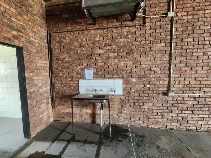 Industrial utility space featuring exposed brick walls, a stainless steel sink with tiled splashback, and an overhead water heater.
