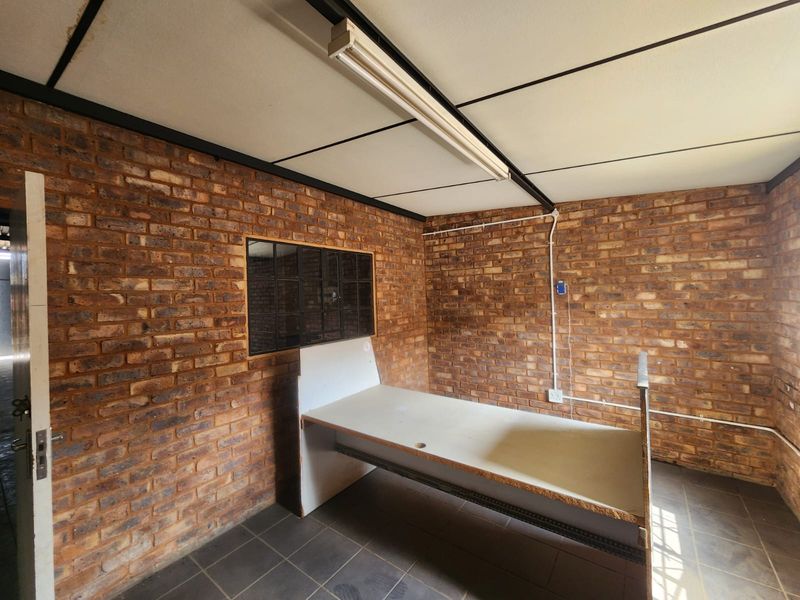 Functional industrial-style office space featuring exposed brick walls, tiled flooring, and a built-in desk, suitable for a workshop or administrative area.