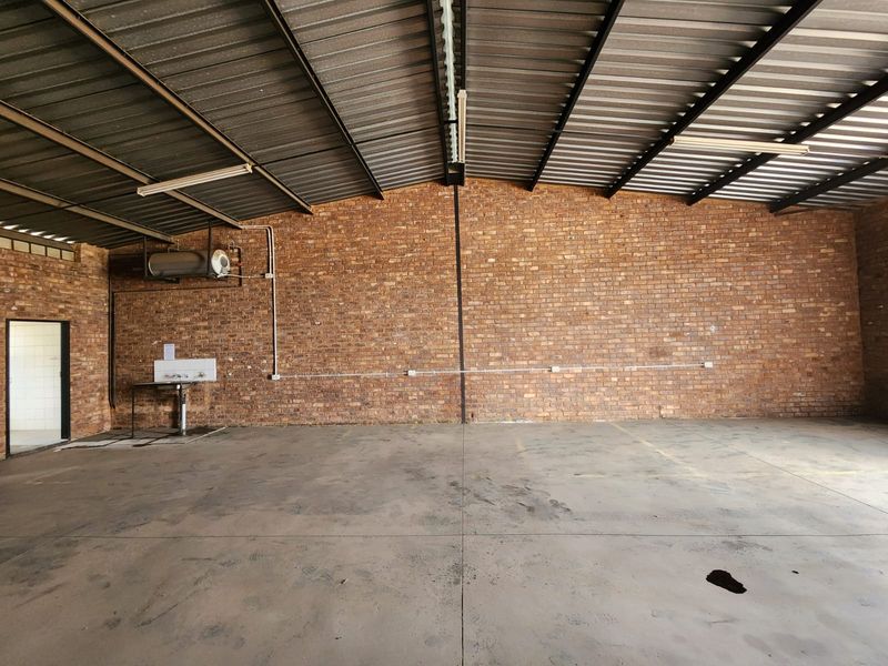 Spacious industrial utility area featuring exposed brick walls, concrete flooring, corrugated metal roofing, and a functional wall-mounted utility sink.