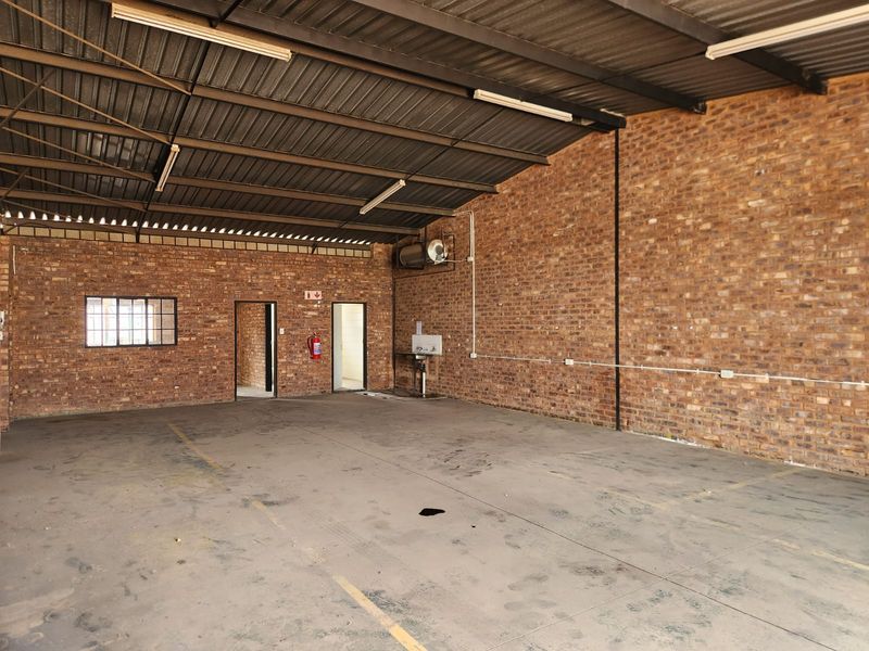 Spacious industrial utility area featuring exposed brick walls, concrete flooring, steel roof trusses, and a wall-mounted basin with an integrated geyser.