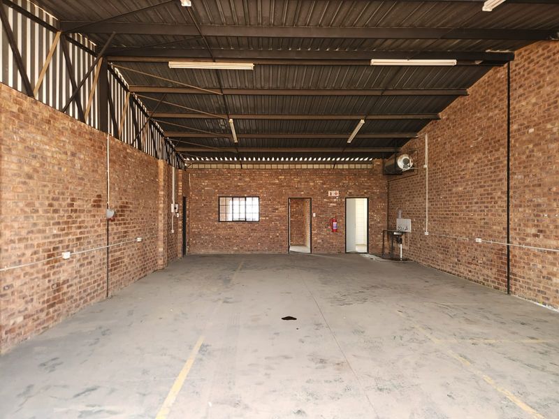 Spacious industrial utility area featuring exposed brick walls, high steel truss ceilings, concrete flooring, and basic utility plumbing fixtures.