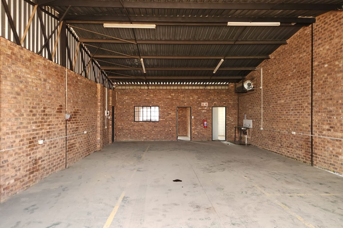 Spacious industrial utility area featuring exposed brick walls, high steel truss ceilings, concrete flooring, and basic utility plumbing fixtures.