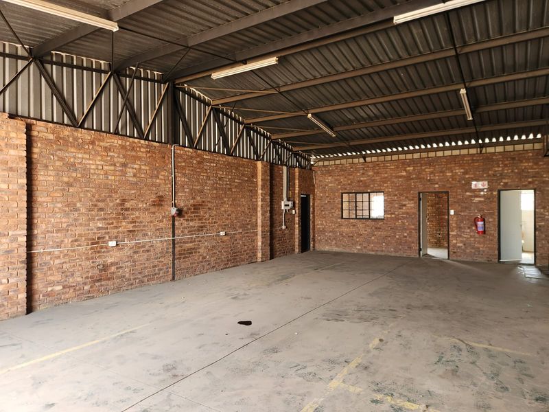 Spacious industrial utility area featuring exposed brick walls, high corrugated metal roofing, and durable concrete flooring, suitable for various commercial or storage applications.