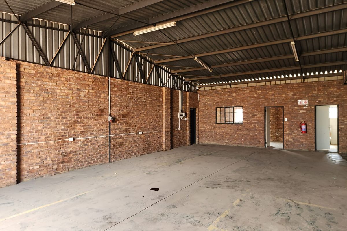 Spacious industrial utility area featuring exposed brick walls, high corrugated metal roofing, and durable concrete flooring, suitable for various commercial or storage applications.