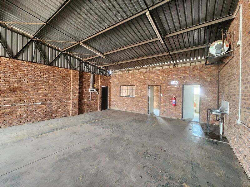 Spacious industrial utility area featuring exposed brick walls, concrete flooring, a metal roof, and a functional wall-mounted sink.