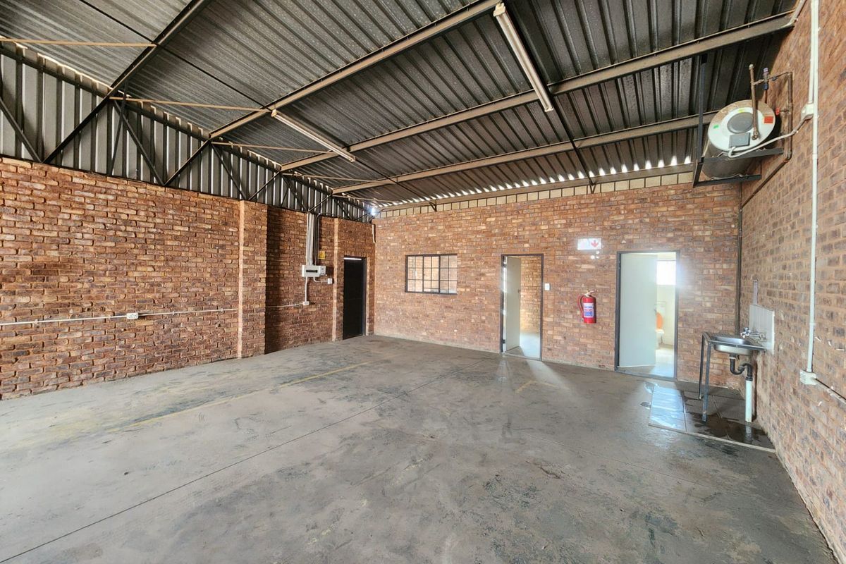 Spacious industrial utility area featuring exposed brick walls, concrete flooring, a metal roof, and a functional wall-mounted sink.