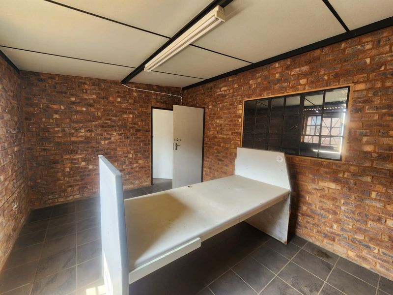 A functional office space featuring exposed brick walls, tiled flooring, built-in desk, and an internal window providing natural light.