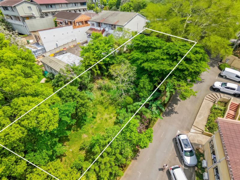 Aerial view of a vacant land plot featuring mature trees and established vegetation, situated within a developed business or residential area.