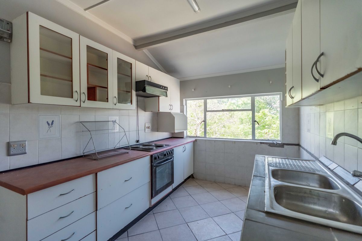 A functional kitchen featuring built-in cabinetry, laminate countertops, a built-in oven with hob, and a double stainless steel sink with tiled backsplash.