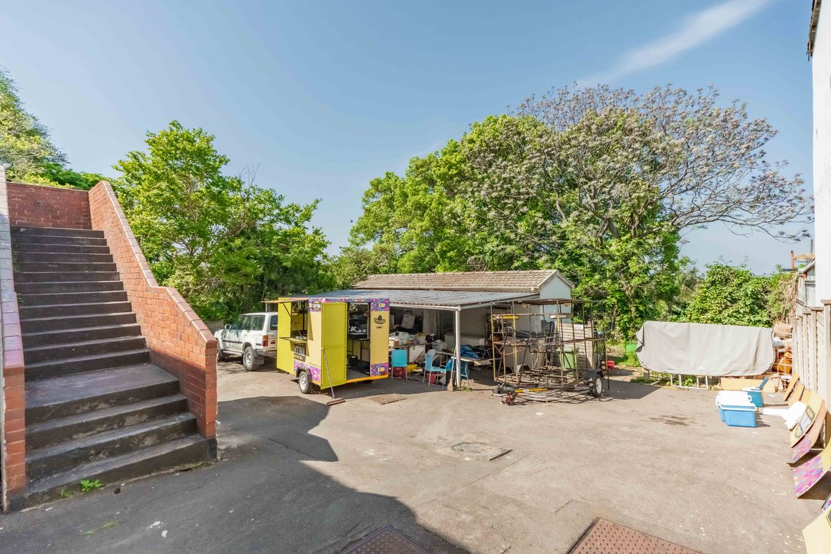 Rear yard area featuring a paved surface, brick staircase, and an open-sided storage structure with a tiled roof.