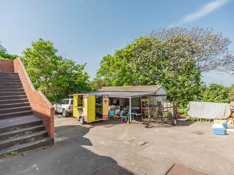 Rear yard area featuring a paved surface, brick staircase, and an open-sided storage structure with a tiled roof.