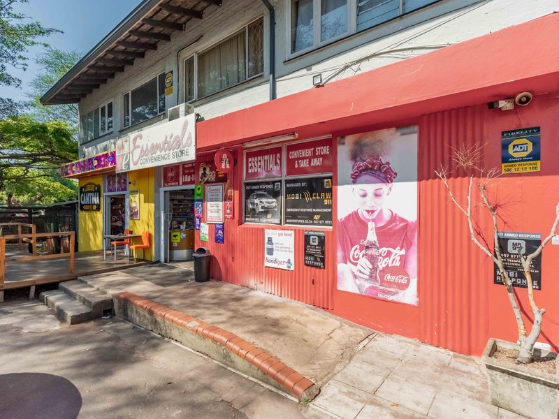 Front facade of a commercial convenience store featuring a corrugated metal exterior, concrete entrance steps, and prominent security and branding signage.