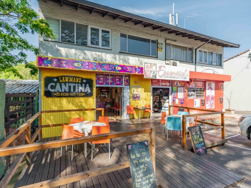 Front facade of a commercial property featuring a timber deck seating area, corrugated metal cladding, and dual storefront signage.