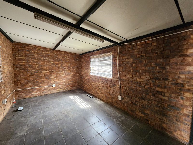 A functional, empty industrial-style office space featuring exposed brick walls, tiled flooring, and exposed steel ceiling beams with integrated lighting.