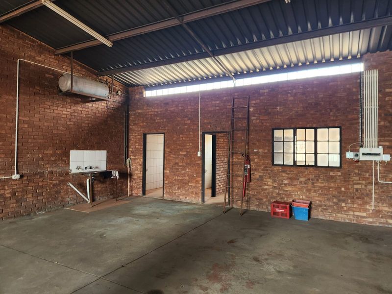 Spacious industrial utility area featuring exposed brick walls, concrete flooring, a wall-mounted sink, and high-clearance corrugated metal roofing.