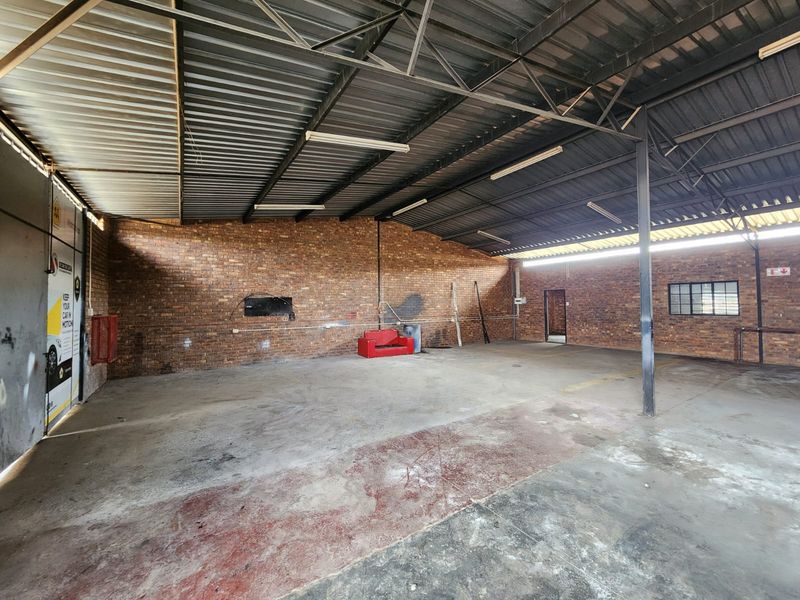 Spacious industrial utility area featuring exposed brick walls, high corrugated metal roofing, and durable concrete flooring, suitable for workshop or storage use.
